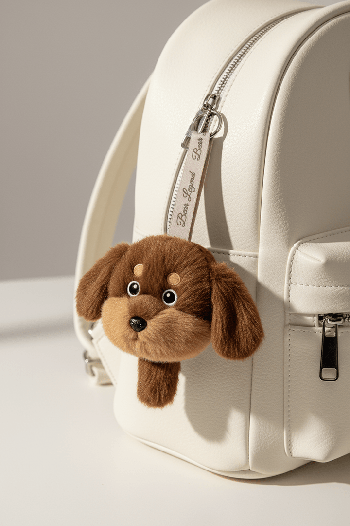 GrinSquid Nneka brown dog plush bag charm clipped to the zip of a cream leather mini backpack via a branded ribbon strap