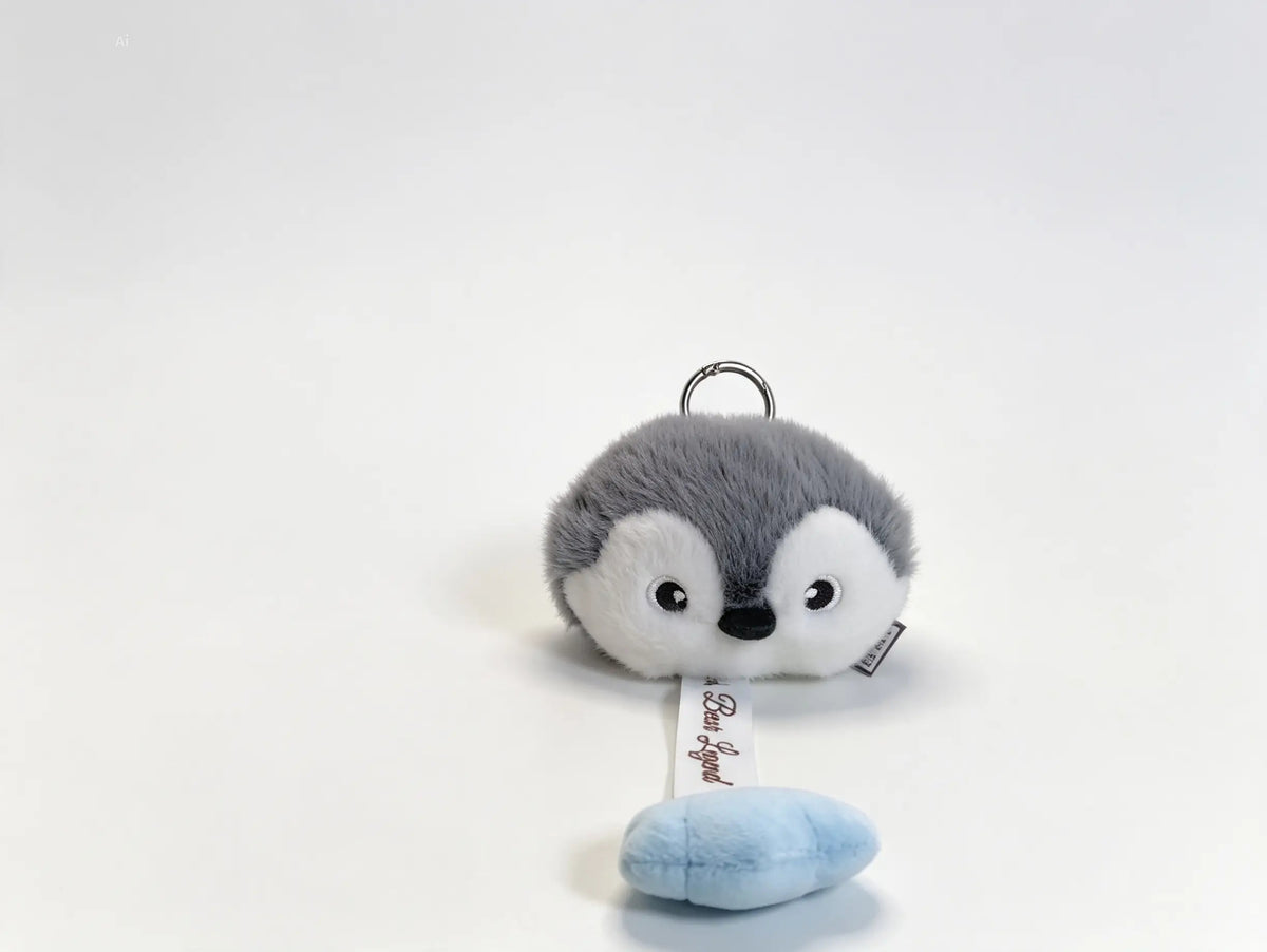 A small plush penguin keychain with a gray and white body, black eyes, and a light blue ice cream cone accessory below, photographed on a clean white background.