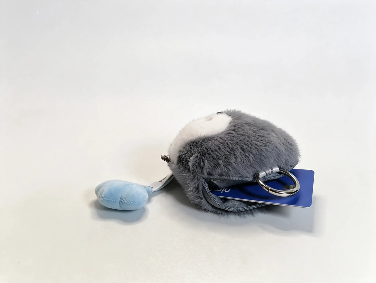 A small plush keychain shaped like a gray and white animal, with a light blue hanging tag and a metal key ring, photographed on a plain light background.