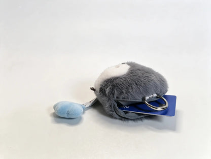 A small plush keychain shaped like a gray and white animal, with a light blue hanging tag and a metal key ring, photographed on a plain light background.