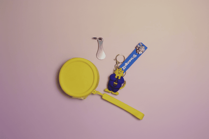 Yellow hand mirror, silver hair clip, and blue keychain with cartoon character on a pink background